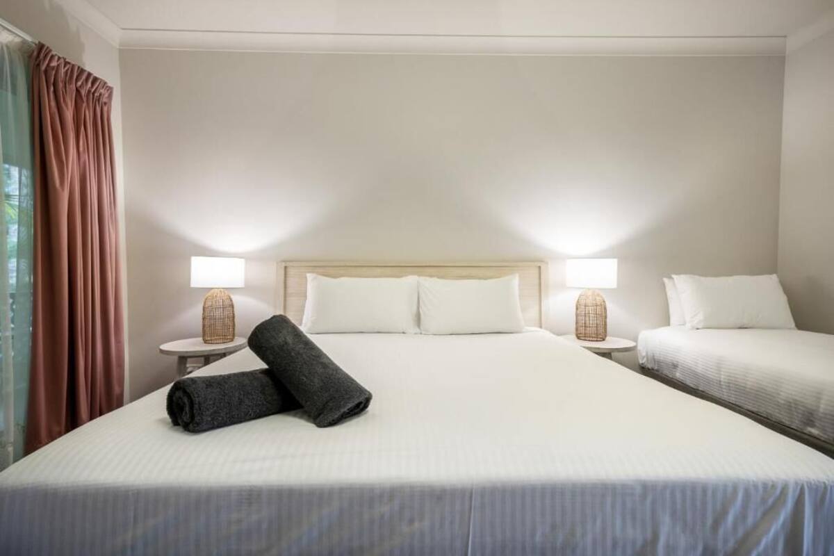 A hotel room with a large bed, two bedside tables with lamps, a headboard, and a window with curtains.