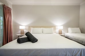 Hotellihuone, jossa on suuri sänky, kaksi yöpöytää valaisimineen, sängynpääty ja ikkuna, jossa on verhot.
