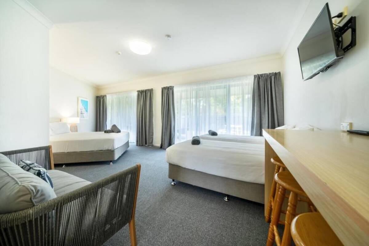 A hotel room with two beds, a desk, a chair, and a TV mounted on the wall.