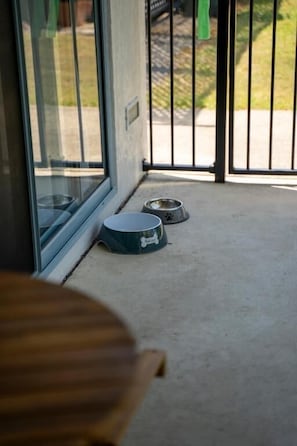 Parvekkeessa on betonilattia, kaksi lemmikkieläinten ruokakuppia ja puinen pöytä.