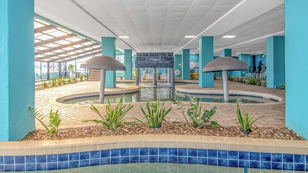 Un área de piscina con una fuente central, suelo de baldosas y pilares azules.