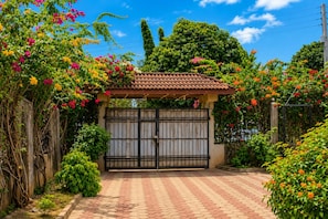 Una entrada porticada con techo de tejas, rodeada de exuberante vegetación y plantas en flor.