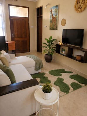 A room with a sofa, a television, a potted plant, and a door. - Maisha Garden  (Dar es Salaam)