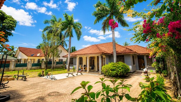 Un patio con palmeras, un espacio de estar techado y un edificio con techo de tejas.