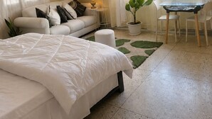 Un dormitorio con cama, sofá, mesa con sillas, planta en maceta y un cuadro en la pared.