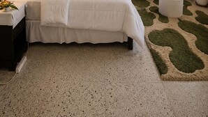 Un dormitorio con cama, mesita de noche, sofá, mesa de centro, un ventilador de techo, una ventana con cortinas y una planta en maceta.