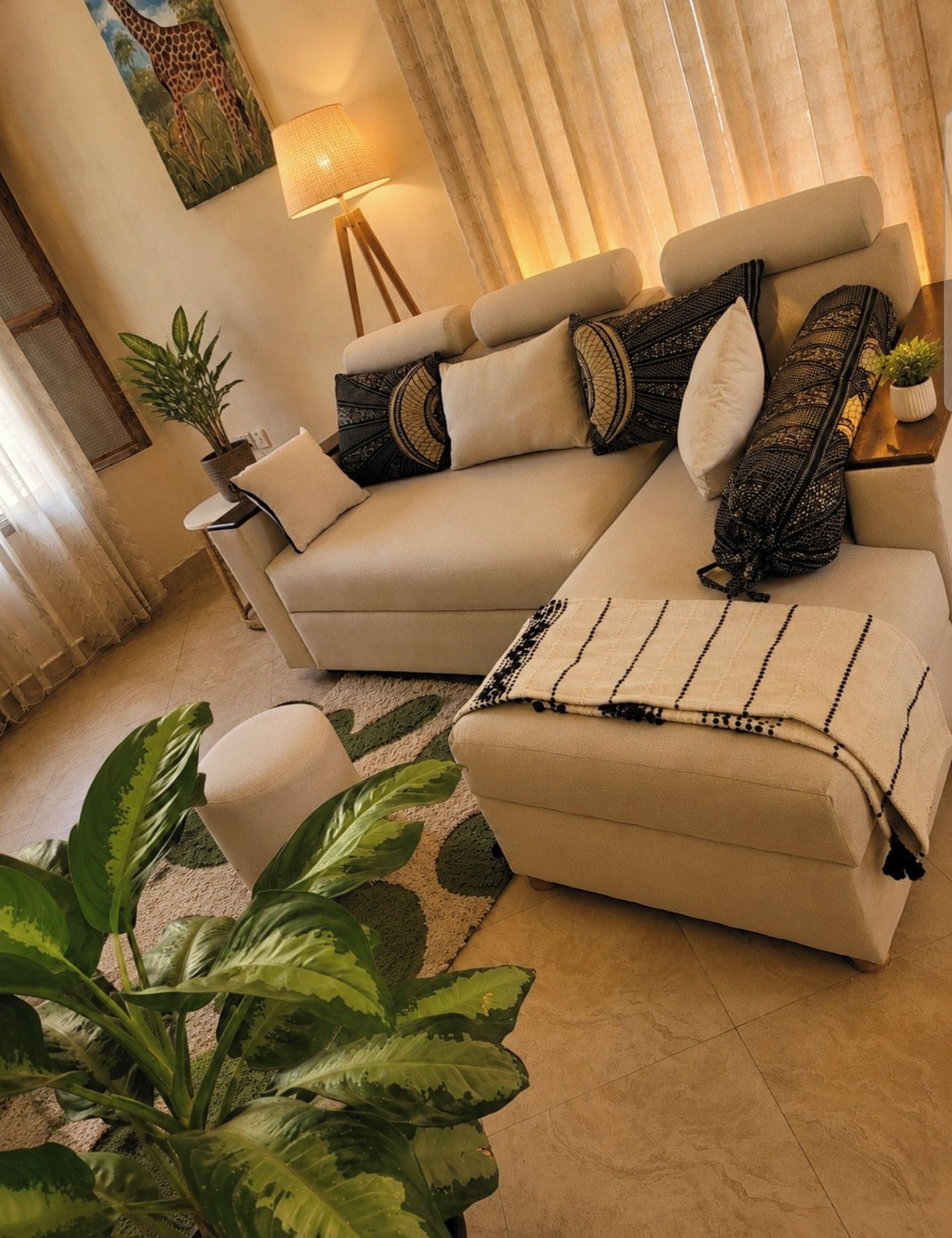 Una sala de estar con un sofá color beige, cojines estampados, una lámpara de pie y plantas verdes.