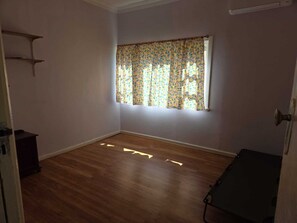 A room with wooden flooring, a window with patterned curtains, and a door with a handle.