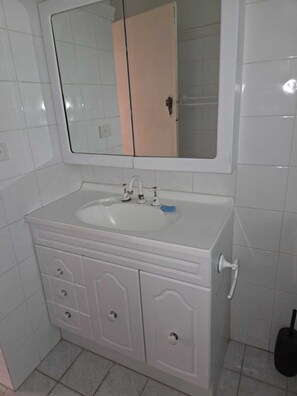 Une salle de bain avec un lavabo blanc, un miroir au-dessus et des toilettes sur la droite.
