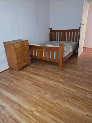 Une pièce avec un lit en bois, une commode en bois et une porte.