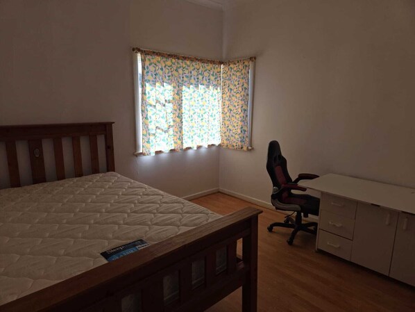 Une chambre à coucher avec un lit, un bureau, une chaise et une fenêtre ornée de rideaux à motifs.