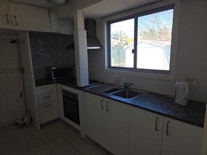 A kitchen with white cabinets, a microwave, a sink, and a window with a view of a house.