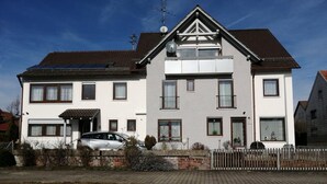 A two-story residential building with a central balcony, a car parked in the driveway, and a clear sky. - Pension Merkle (Ichenhausen)