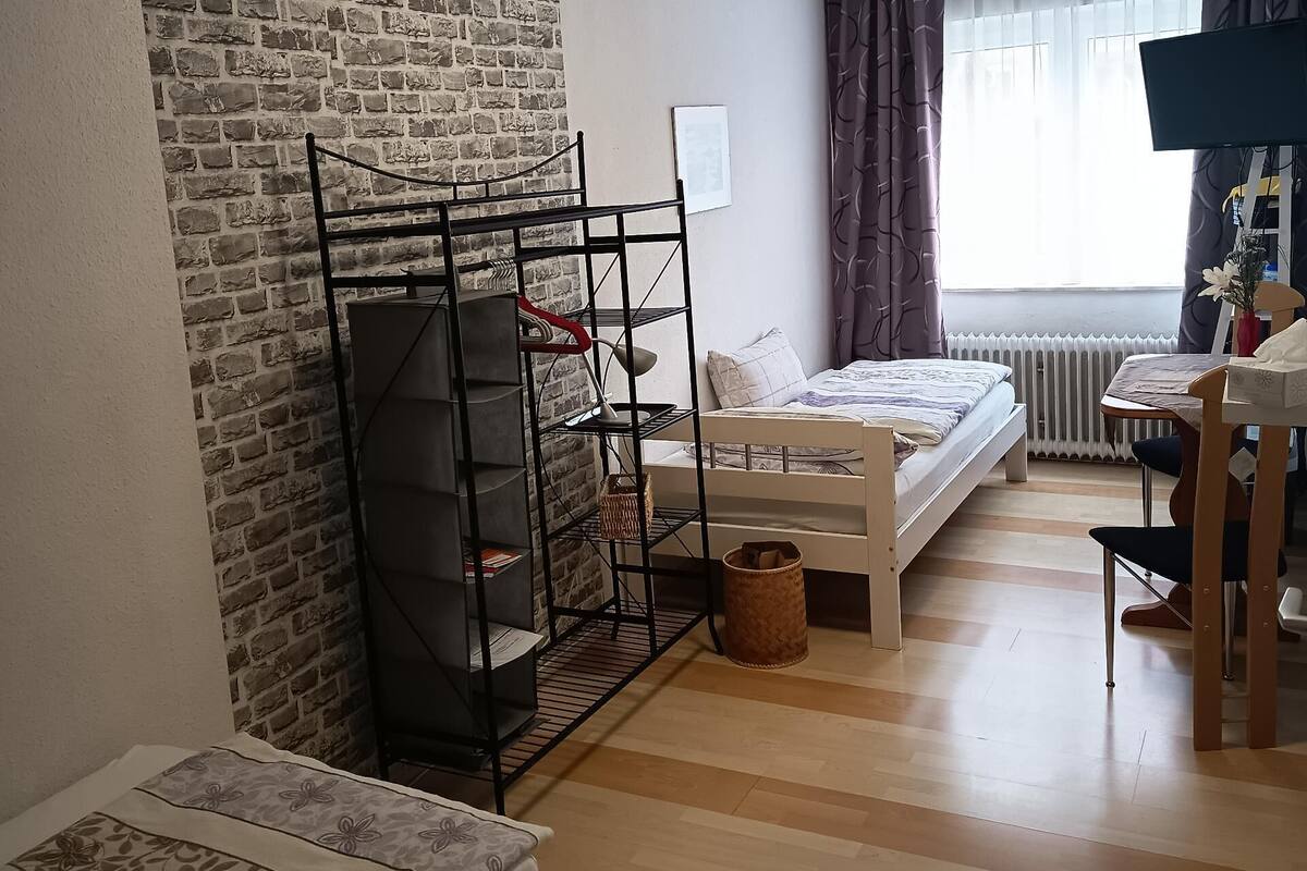 A room with a brick wall, a bunk bed, a desk with a chair, and a radiator.