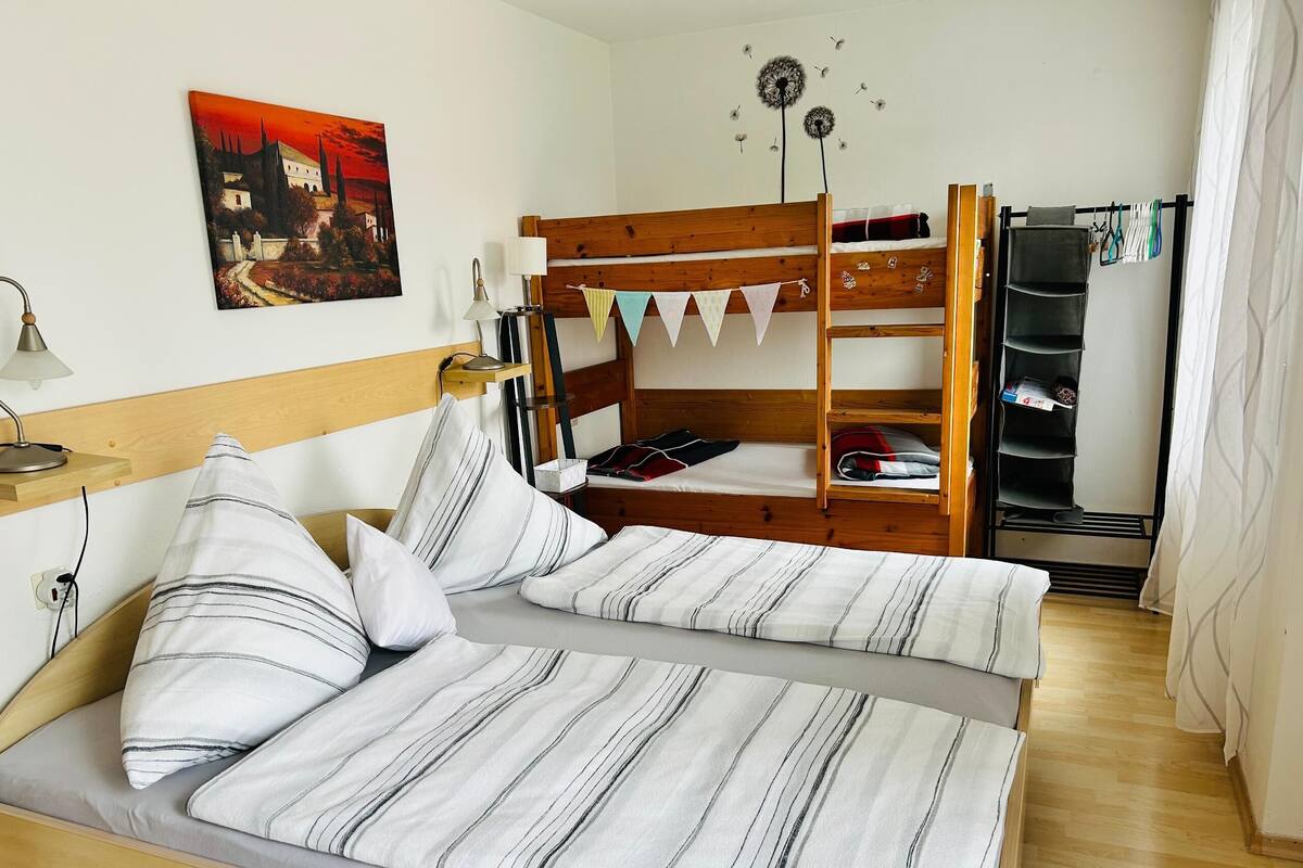 A room with a bunk bed, a bedside table with a lamp, a wall-mounted shelf, and a painting.