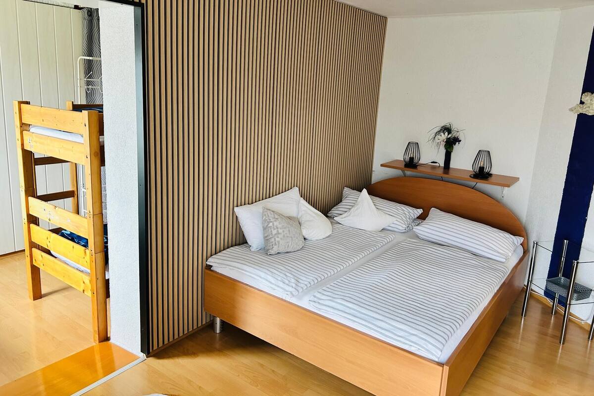 A modern bedroom with a wooden bed, a wooden ladder, and a striped wall panel.
