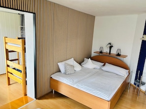 A modern bedroom with a wooden bed, a wooden ladder, a striped pillow, and a small shelf with decorative items.