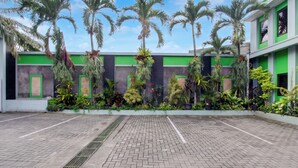 A courtyard with a paved walkway, palm trees, and a building with green and grey walls. - Townhouse Oak Pancanaka Malioboro Hotel (Kasihan)