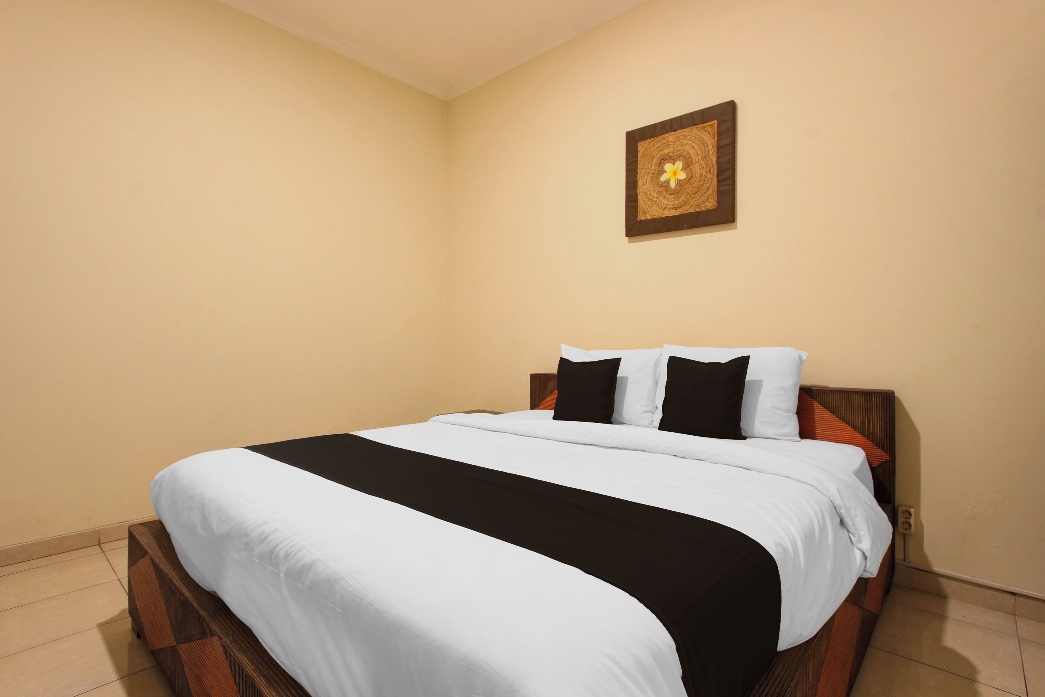 A neatly made bed with a wooden headboard, a wall-mounted artwork, and a tiled floor.