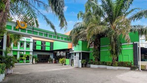 A modern building with a green facade, a paved entrance, and surrounding palm trees. - Townhouse Oak Pancanaka Malioboro Hotel (Kasihan)