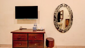 A wooden dresser with drawers, a flat-screen TV mounted above it, a decorative mirror with an ornate frame, and a small stool. - Townhouse Oak Pancanaka Malioboro Hotel (Kasihan)