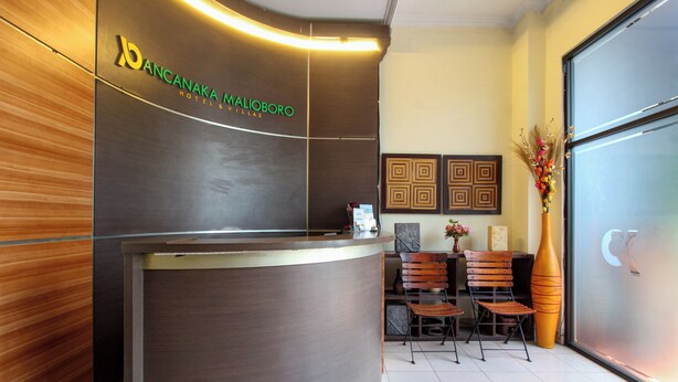 A reception desk with a logo, a waiting area with chairs, and a large vase with flowers. - Townhouse Oak Pancanaka Malioboro Hotel (Kasihan)