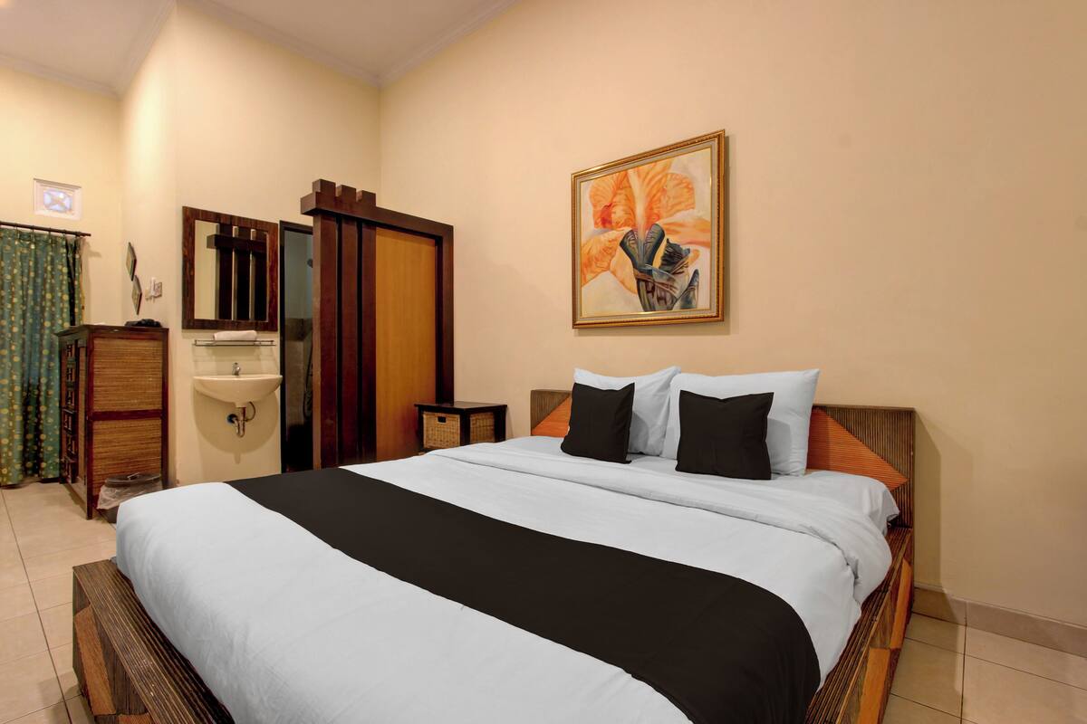 A hotel room with a bed, a sink, a mirror, and a painting on the wall.