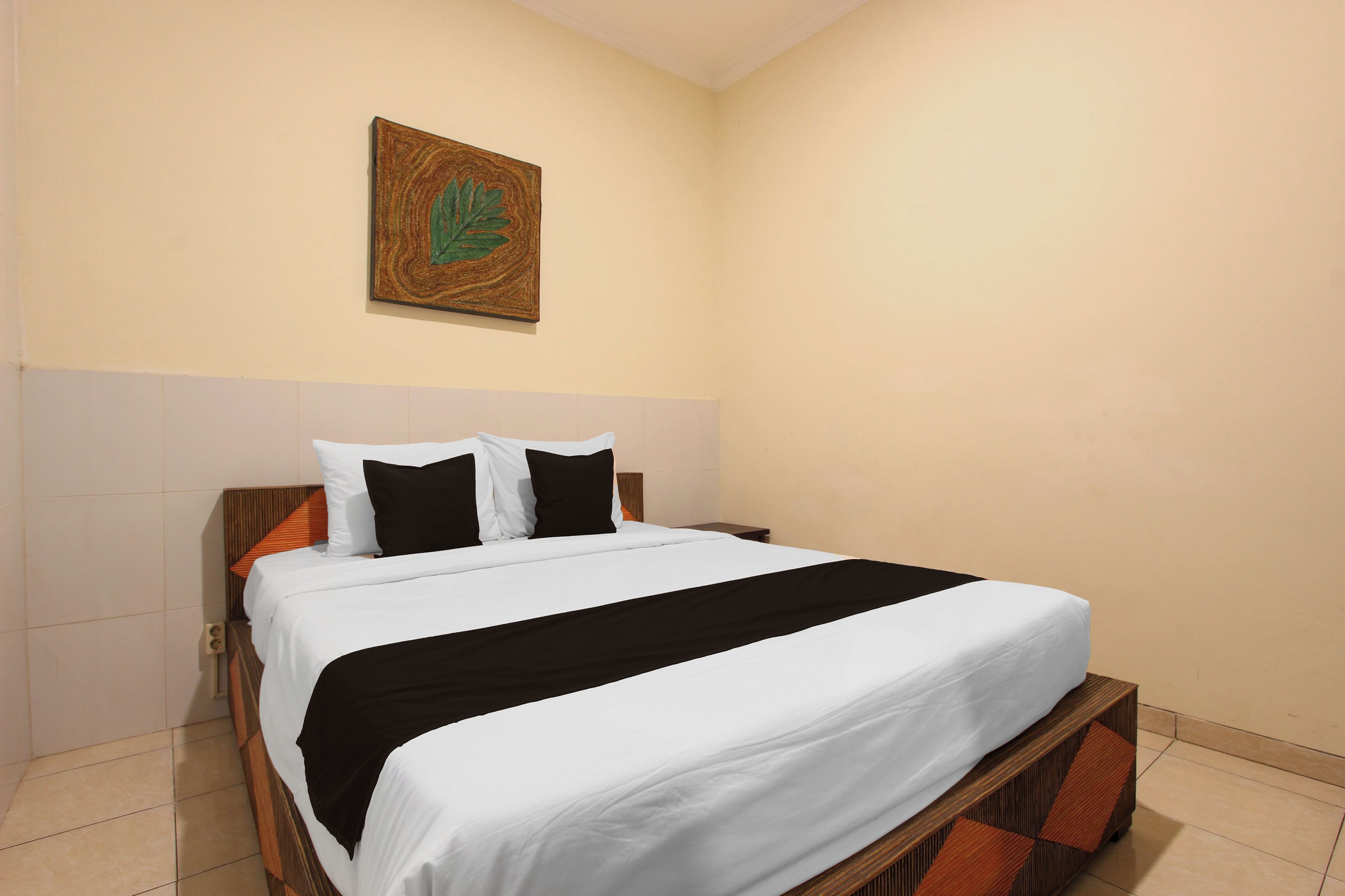 A neatly made bed with white and black bedding, a wooden headboard, and a single wall-mounted artwork.