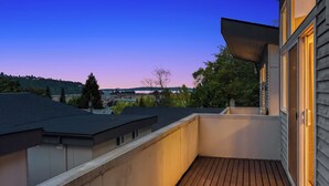 Een balkon met een houten vloer, uitzicht op omliggende gebouwen en een heldere lucht.