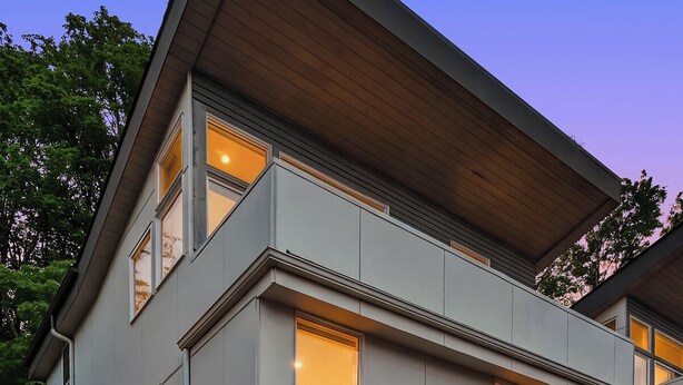 Een modern huis met twee verdiepingen, een plat dak, grote ramen en een goed verlichte entree.
