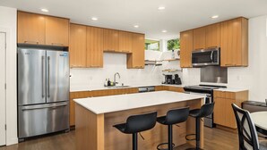 Een moderne keuken met houten kastjes, roestvrijstalen apparatuur en een centraal kookeiland met barstoelen.