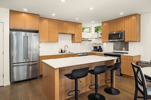 A modern kitchen with wooden cabinets, stainless steel appliances, and a central island with bar stools. - Modern 3BR/2BA Seattle Home: Spacious, Family-Friendly & Parking Included (Seattle)