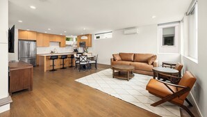 Een moderne keuken met een ingebouwde oven, een eethoek met tafel en stoelen, een leren bank en een aan de muur bevestigde televisie.