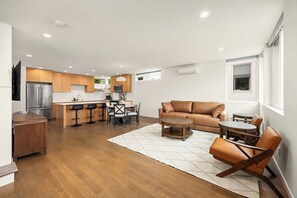 A modern kitchen with a built-in oven, a dining area with a table and chairs, a leather sofa, and a TV mounted on the wall. - Modern 3BR/2BA Seattle Home: Spacious, Family-Friendly & Parking Included (Seattle)