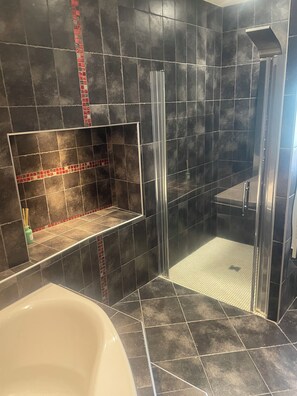 Une salle de bain avec une baignoire, une douche dotée d’une porte en verre et un mur carrelé avec une bordure rouge.