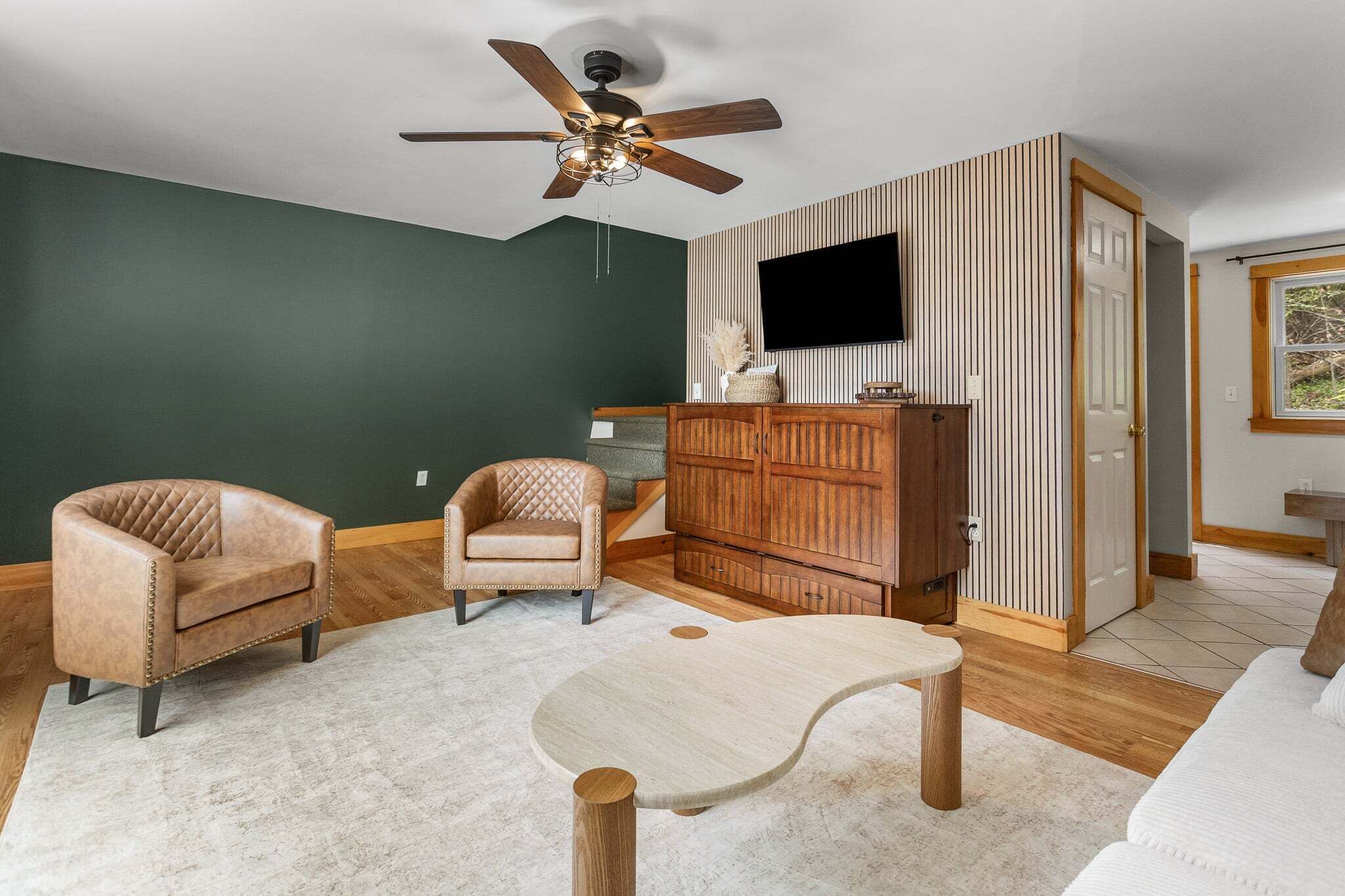 A living room with a ceiling fan, a TV, a wooden cabinet, and a white sofa.