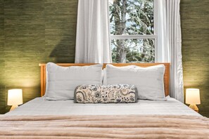 A bed with white linens, a patterned pillow, and a window with curtains.
