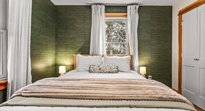 Un dormitorio con cama, dos lámparas de noche, una ventana con cortinas y una puerta.