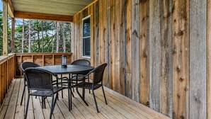 A covered outdoor area with a wooden deck, a round table with chairs, and a window. - Fern Cottage - NEW Cottage in Blue Hill! (Blue Hill)