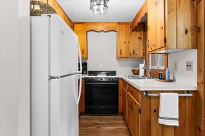 A compact kitchen with wooden cabinets, a white refrigerator, a stove, and a sink.