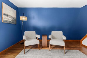 A room with two chairs, a floor lamp, a small wooden table, and a painting on the wall.