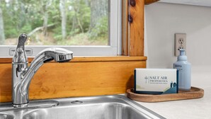 A kitchen with a stainless steel sink, a wooden countertop, a window with a view of trees, and a bottle of hand soap. - Drift A-Frame - NEW A-Frame in Blue Hill! (Blue Hill)