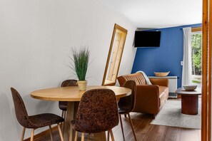 Un comedor con una mesa redonda de madera, dos sillas, una planta en maceta y un televisor montado en la pared.