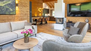 A modern interior with a wooden ceiling, a fireplace, a dining area, and a sofa with a vase of flowers.