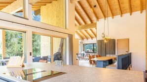 A modern kitchen with a large island, wooden beams, and large windows.