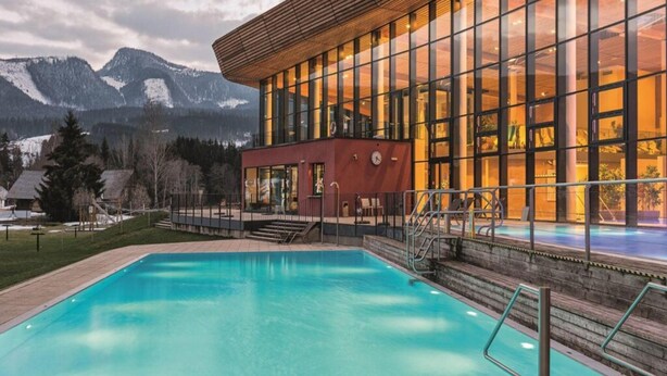 A modern building with a swimming pool, large windows, and a view of mountains.