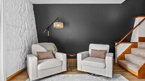 Un salon moderne avec deux fauteuils blancs, une petite table ronde, un lampadaire et un escalier.