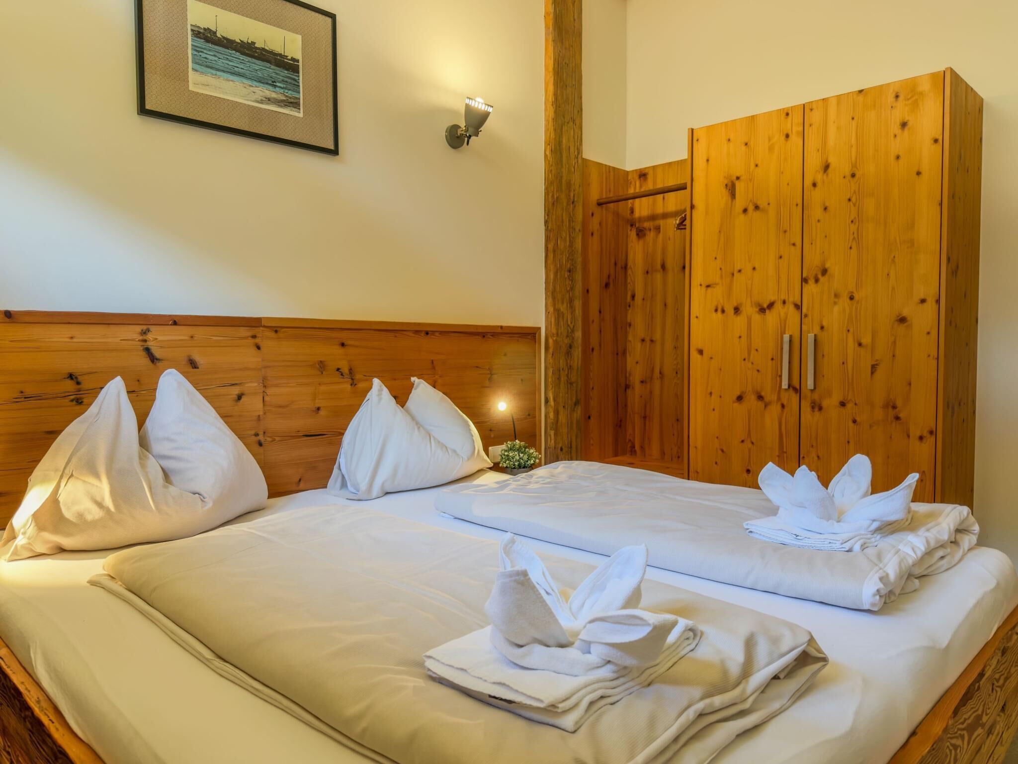 A double bed with white linens, a wooden headboard, a wooden wardrobe, and a framed picture on the wall.