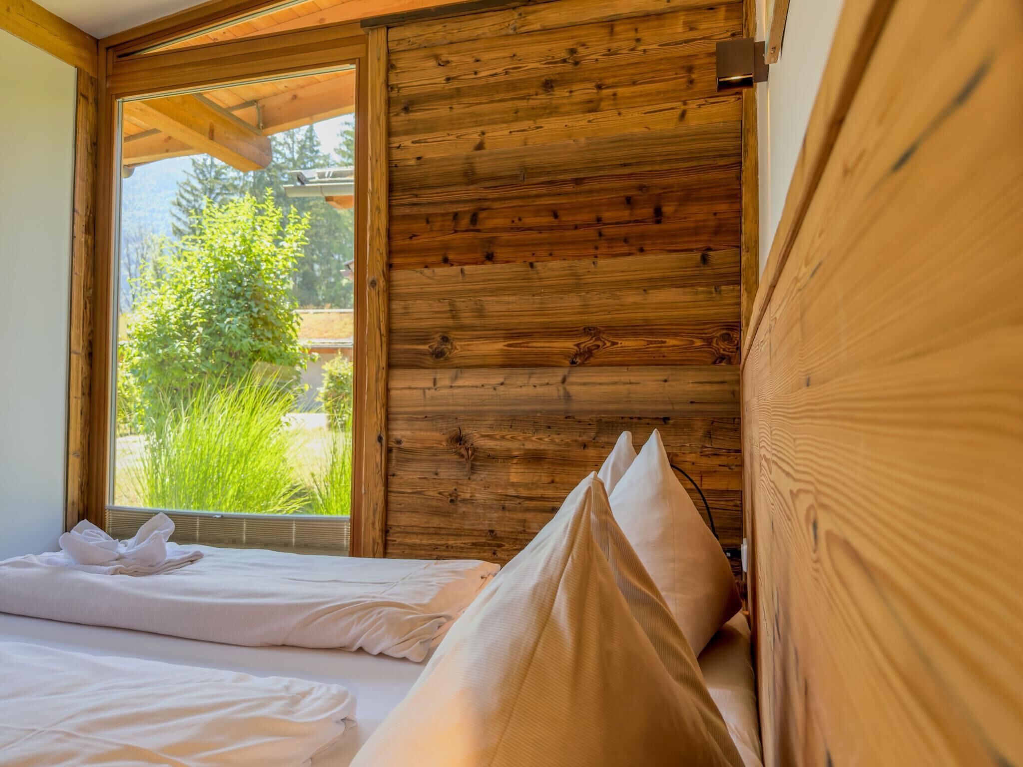 A room with a wooden wall and a window overlooking greenery.