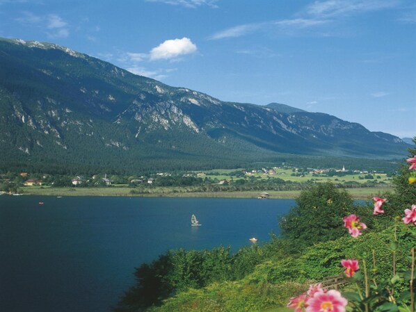 Un lago con montañas al fondo, un bote pequeño y algunas casas cerca de la orilla.